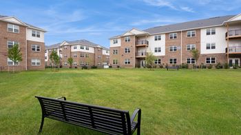 A black bench sits in the grass in front of apartment buildings.